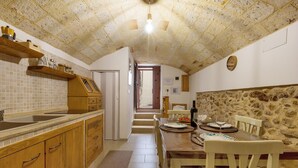 A kitchen with wooden cabinets, a tiled backsplash, and a stone wall. There is a dining table with chairs and a bottle of wine. - 3693 Casa Relax by Barbarhouse (Mesagne)