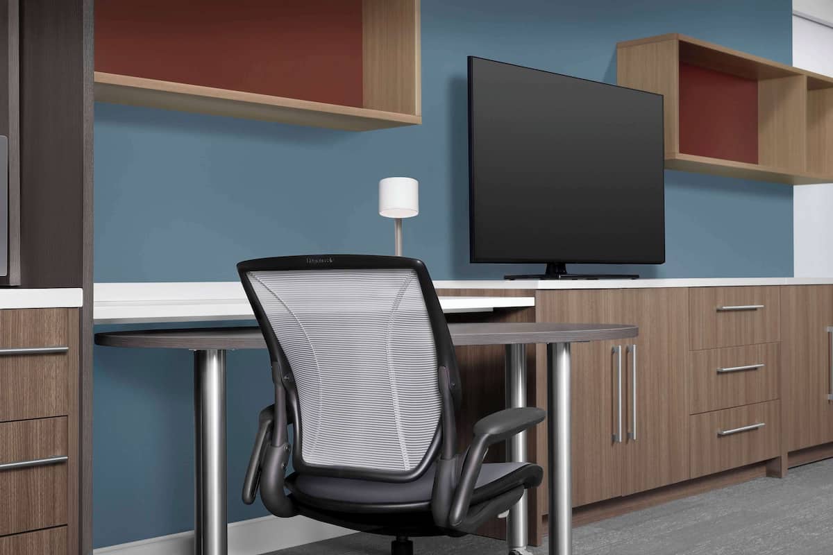 Un espace de bureau moderne comprenant un bureau, une chaise, un téléviseur et des étagères en bois.