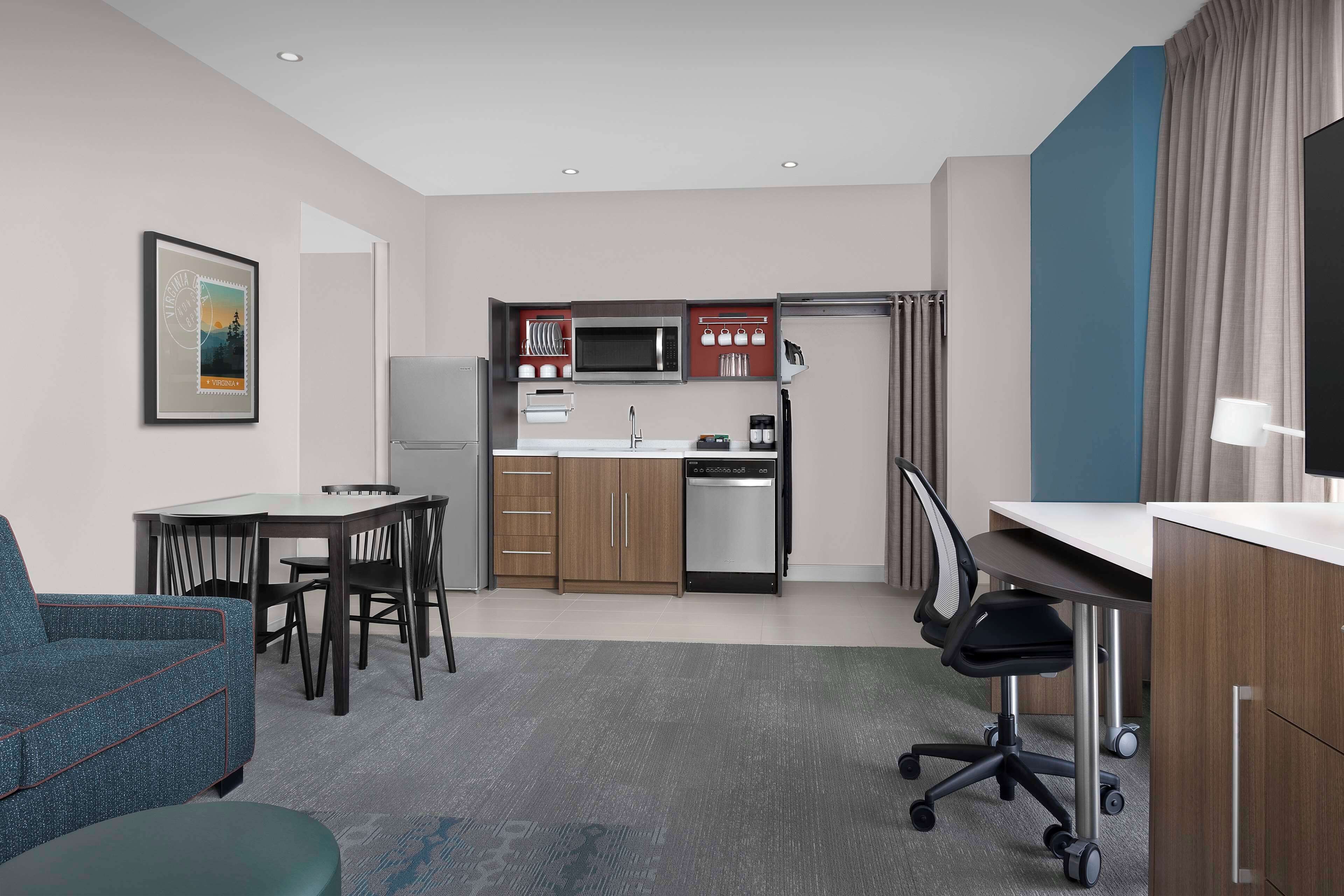 A compact hotel room with a kitchenette, a dining area, a sofa, and a desk.