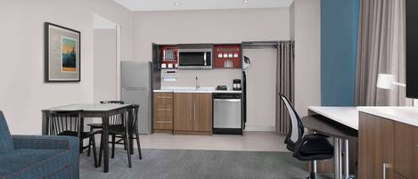 A compact hotel room with a kitchenette, a dining area, a sofa, and a desk.