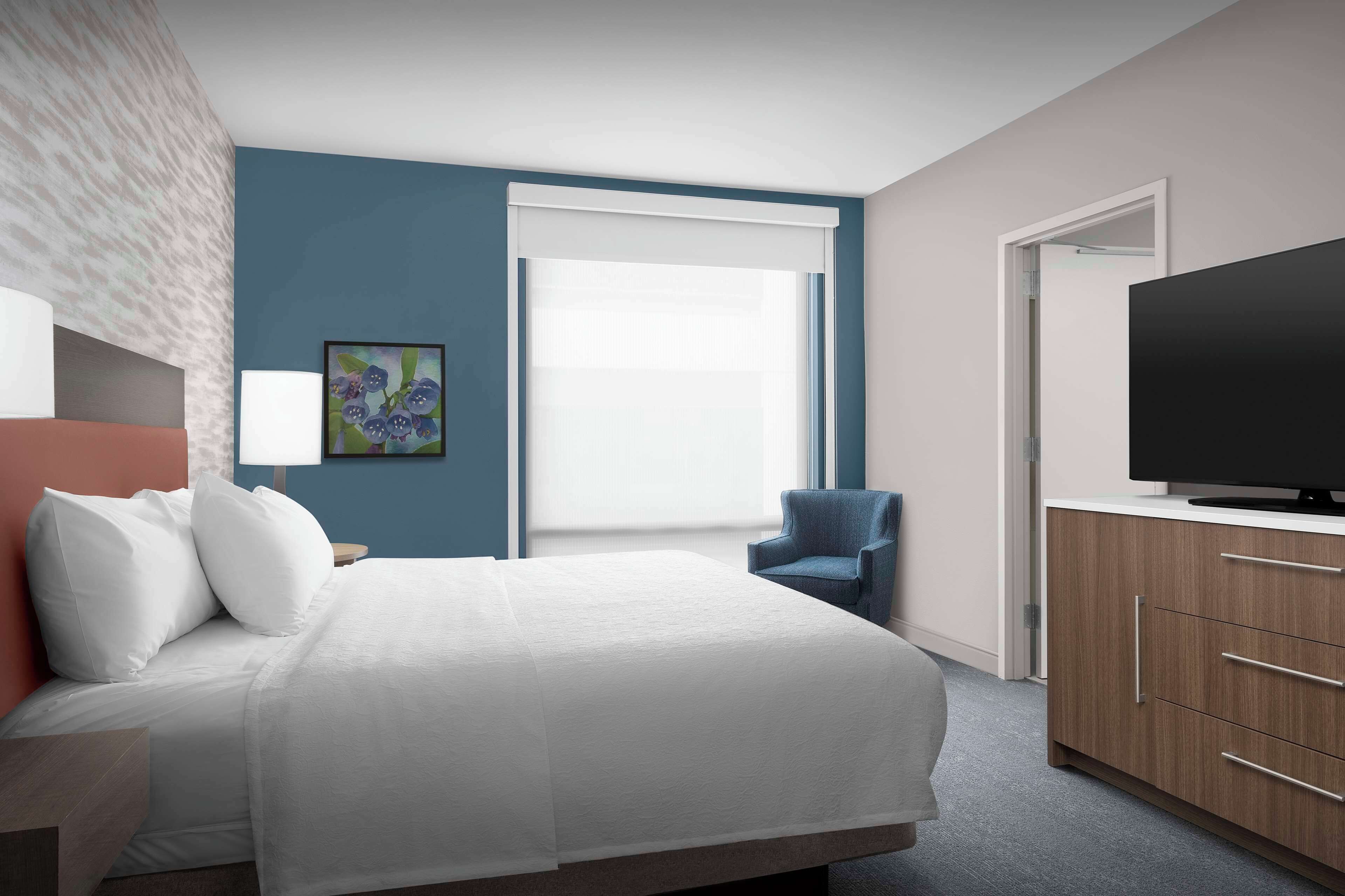 A hotel room with a bed, a chair, a TV, and a cabinet.