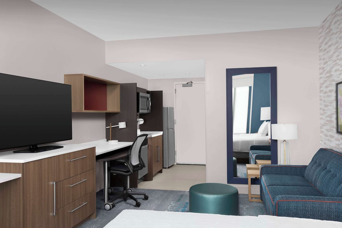 Une chambre d’hôtel équipée d’un lit, d’un bureau avec un ordinateur, d’une télévision à écran plat, d’un four à micro-ondes, d’un réfrigérateur, d’un canapé et d’un miroir.