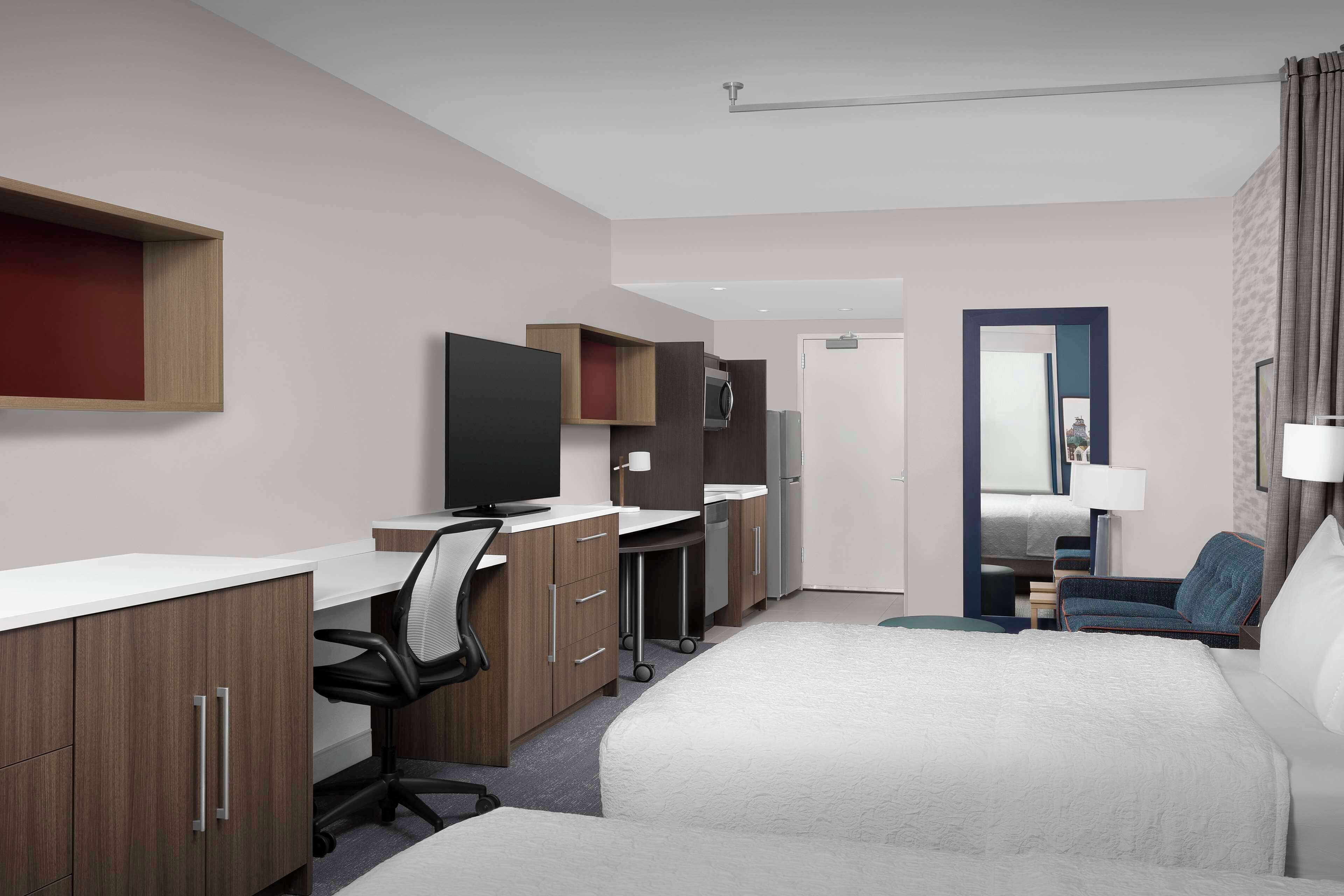 Una habitación de hotel con cama, escritorio con silla, televisión y baño visible a través de una puerta abierta.