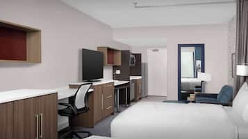Una habitación de hotel con cama, escritorio con silla, televisión y baño visible a través de una puerta abierta.