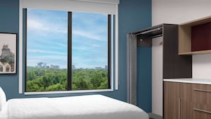 Une chambre avec une grande fenêtre, un lit, une armoire et un tableau encadré au mur.