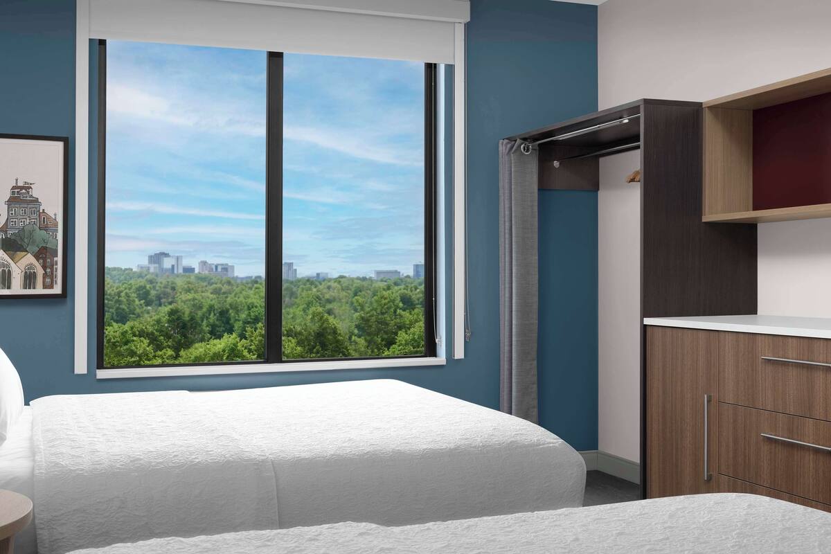 Une chambre avec une grande fenêtre, un lit, une armoire et un tableau encadré au mur.
