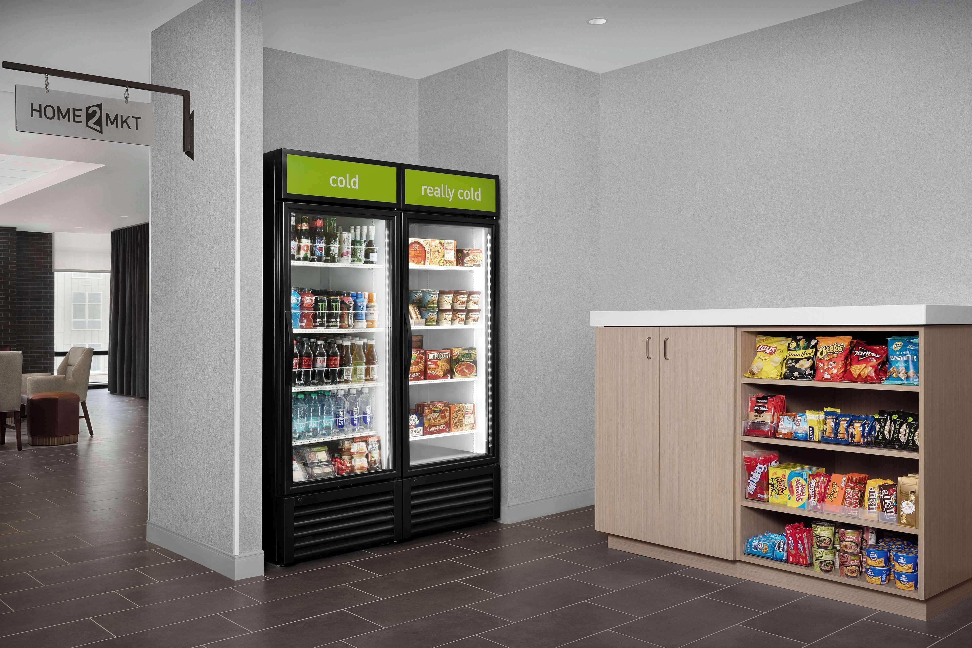 A hotel lobby with a cold and really cold beverage refrigerator, snack shelves, and a sign indicating the home and mkt area.