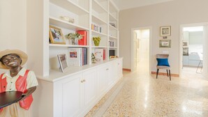 A hotel lobby with a white reception desk, a statue, a bookshelf with books and decorative items, and a chair. - Casa Arnolfo in Lucca (Lucca)