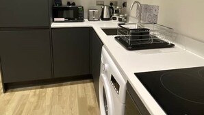 A modern kitchen with grey cabinets, a built-in microwave, a kettle, a toaster, and a washing machine.