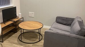 A modern living room with a grey sofa, a wooden coffee table, and a TV on a wooden stand.