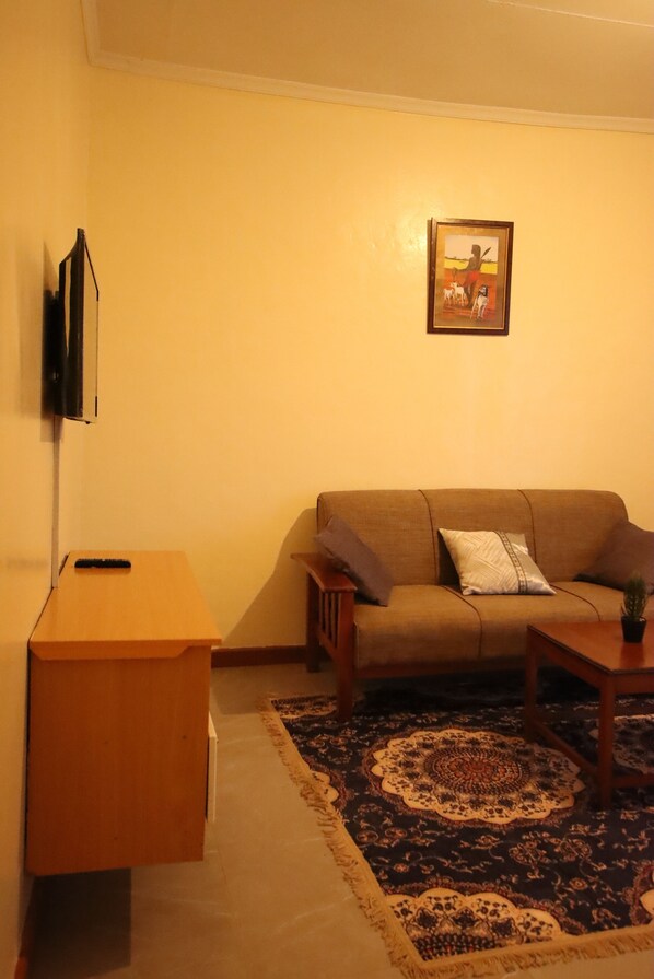 A living room with a sofa, a coffee table, a TV mounted on the wall, and a patterned rug.