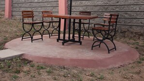 En terrasse med et bord og stole under en stribet parasol, en stenvæg og en bygning i baggrunden.