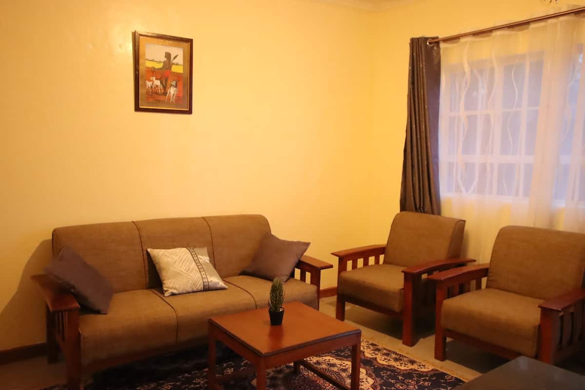 Uma sala de estar com um sofá, duas poltronas, uma mesa de centro e uma janela com cortinas.