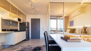 Een moderne hotelkamer met een keukenhoek, een eettafel en een groot raam met uitzicht op de stad.