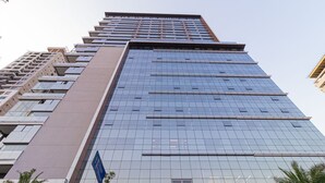 Een hoog gebouw met een moderne glazen gevel, meerdere verdiepingen en een opvallende ingang aan de voet ervan.