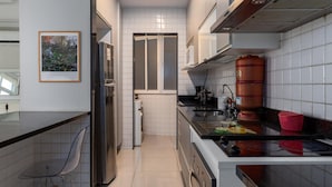 Una cocina moderna con paredes de azulejos blancos, electrodomésticos de acero inoxidable y una encimera negra.