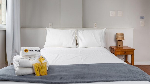 Una habitación de hotel con cama, mesita de noche, lámpara y ventana con cortinas.