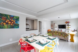 Un coin repas avec une table dressée pour quatre personnes, des chaises et une cuisine en arrière-plan.