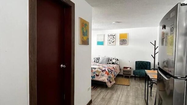 A compact living space with a kitchenette, a bed with patterned bedding, a small dining area, and a door leading to another room. - Cozy Suit!viajeros y Mujeres 100% Seguras!céntrico (Quito)