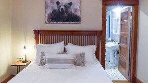 A neatly made bed with white linens and a wooden headboard, a bedside table with a lamp, and a bear-themed artwork on the wall. - Historic, Unique, Walkable, Rail to Denver, Red Rocks (Arvada)