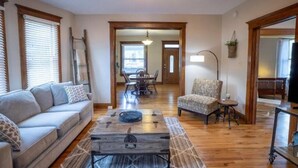 A living room with a sofa, a coffee table, and a chair. There is a dining table with chairs in the background. - Historic, Unique, Walkable, Rail to Denver, Red Rocks (Arvada)