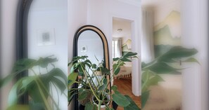 Corredor com um espelho grande, uma planta e uma porta que dá para outro quarto.