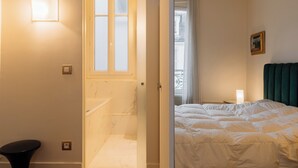 A hotel room with a bathroom, a bed, a window, and a door.