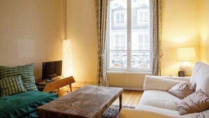 A living room with a sofa, a bench, a television, and a window with curtains.