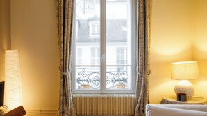 A hotel room with a large window, a radiator, a bedside lamp, and a bed.