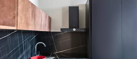 A modern kitchen with a black tiled backsplash, a red sink, and a black refrigerator.