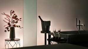 Et værelse med et lille rundt bord, en vase med tørrede blomster, en champagneflaske og to glas.