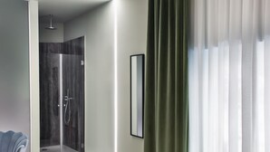 Et moderne hotelværelse med bruser, seng, spisebord og bakke med mad, samt et stort vindue med gardiner.