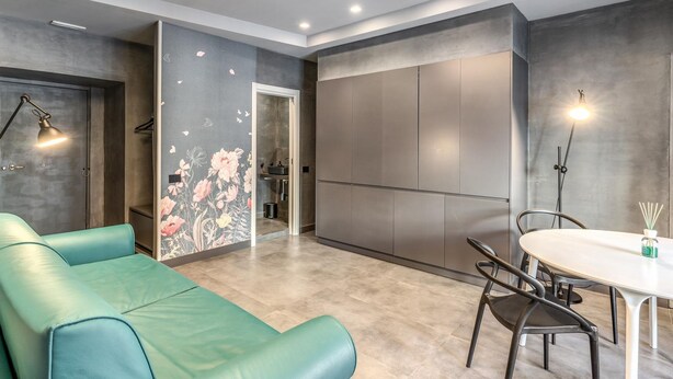 A modern living room with a teal sofa, a dining table with chairs, and a kitchen area visible through an open door. - Green Diamond in Naples (Naples)