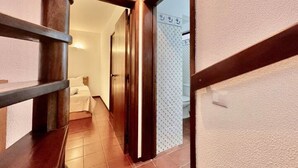 A hallway with a wooden staircase, a bed, and a bathroom with patterned tiles. - 1bedroom duplex beach apartment (Carvoeiro)