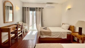A hotel room with a bed, a desk, a chair, a mirror, and a window with curtains. - 1bedroom duplex beach apartment (Carvoeiro)