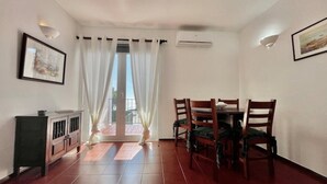 A room with a dining table and chairs, a cabinet, and a large window with curtains. - 1bedroom duplex beach apartment (Carvoeiro)