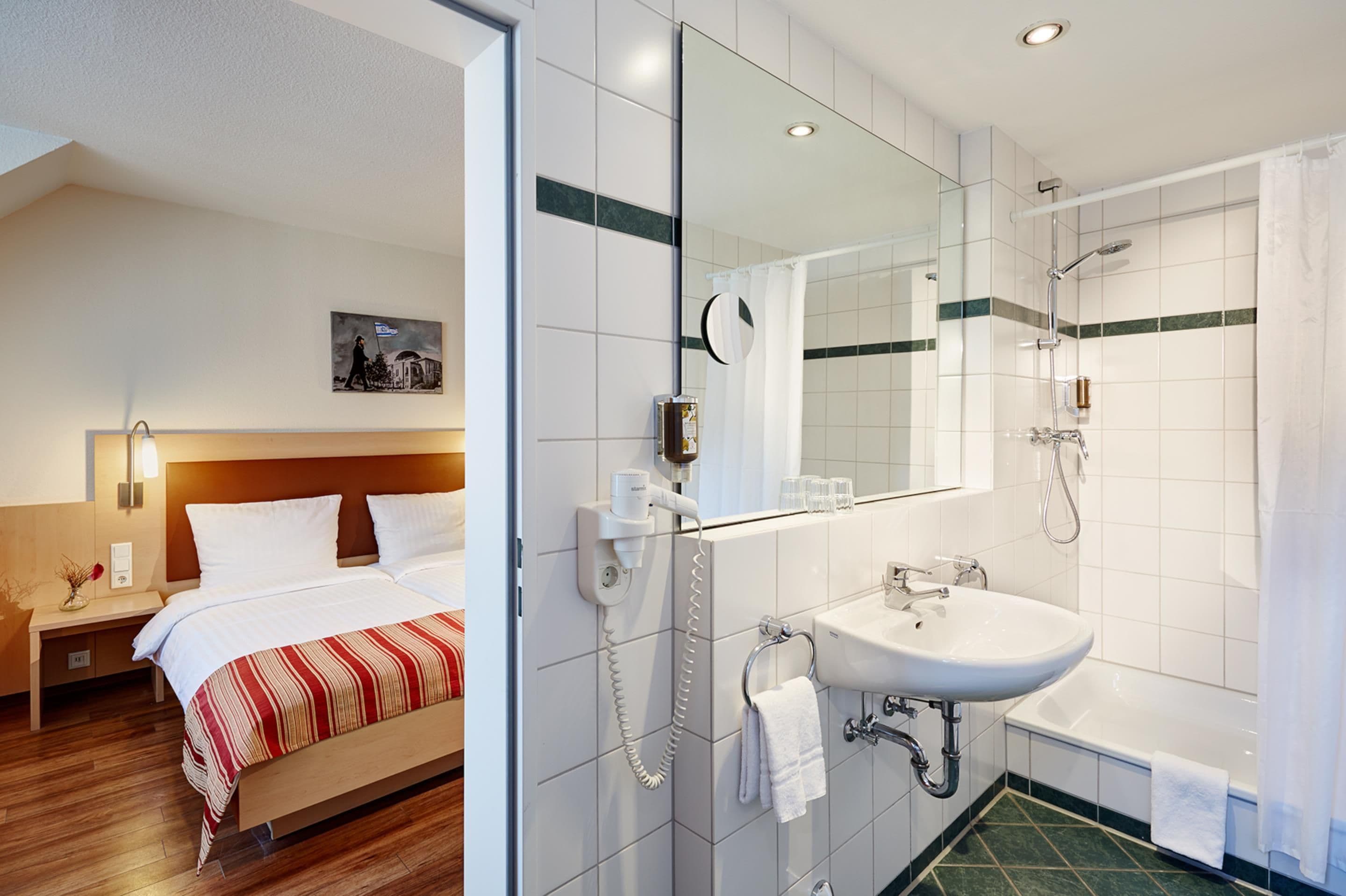 A hotel room with a bed, bedside table, lamp, and a painting on the wall.