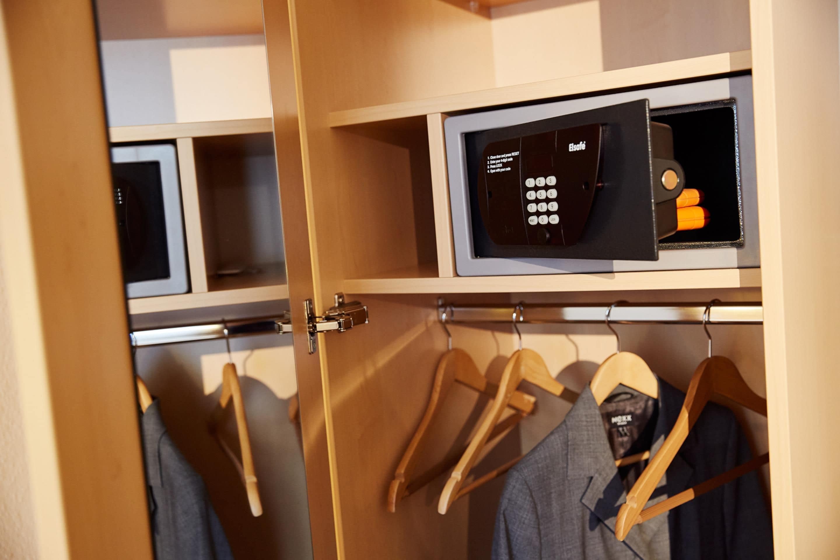 A wardrobe with a microwave on the top shelf and hangers with clothes below.