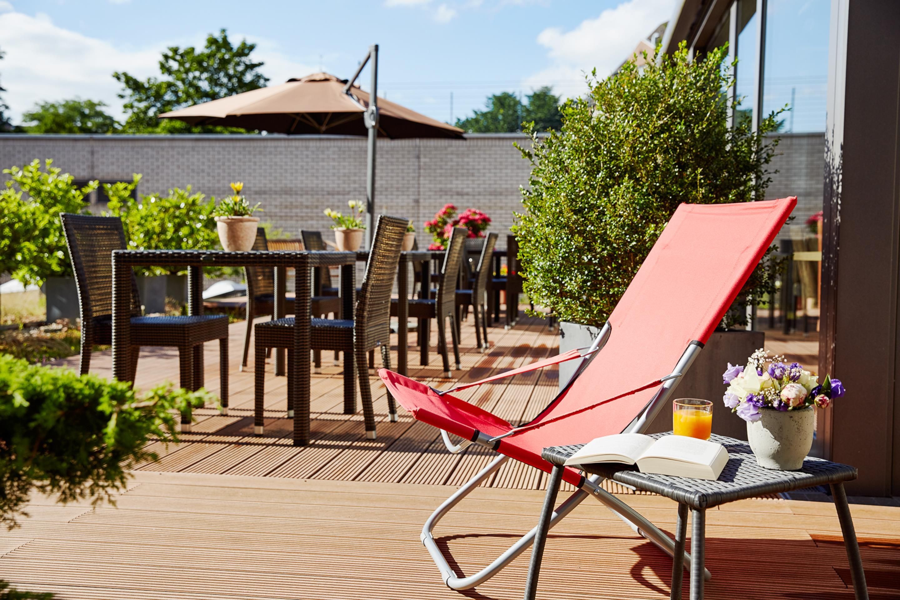 A patio area with wicker furniture, a red lounge chair, and a table with a book and a glass of orange juice.