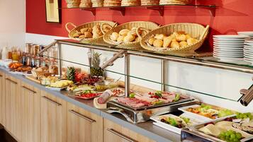 Buffet com diversos alimentos, incluindo pão, frutas e carnes, expostos em balcão com prateleiras de vidro.