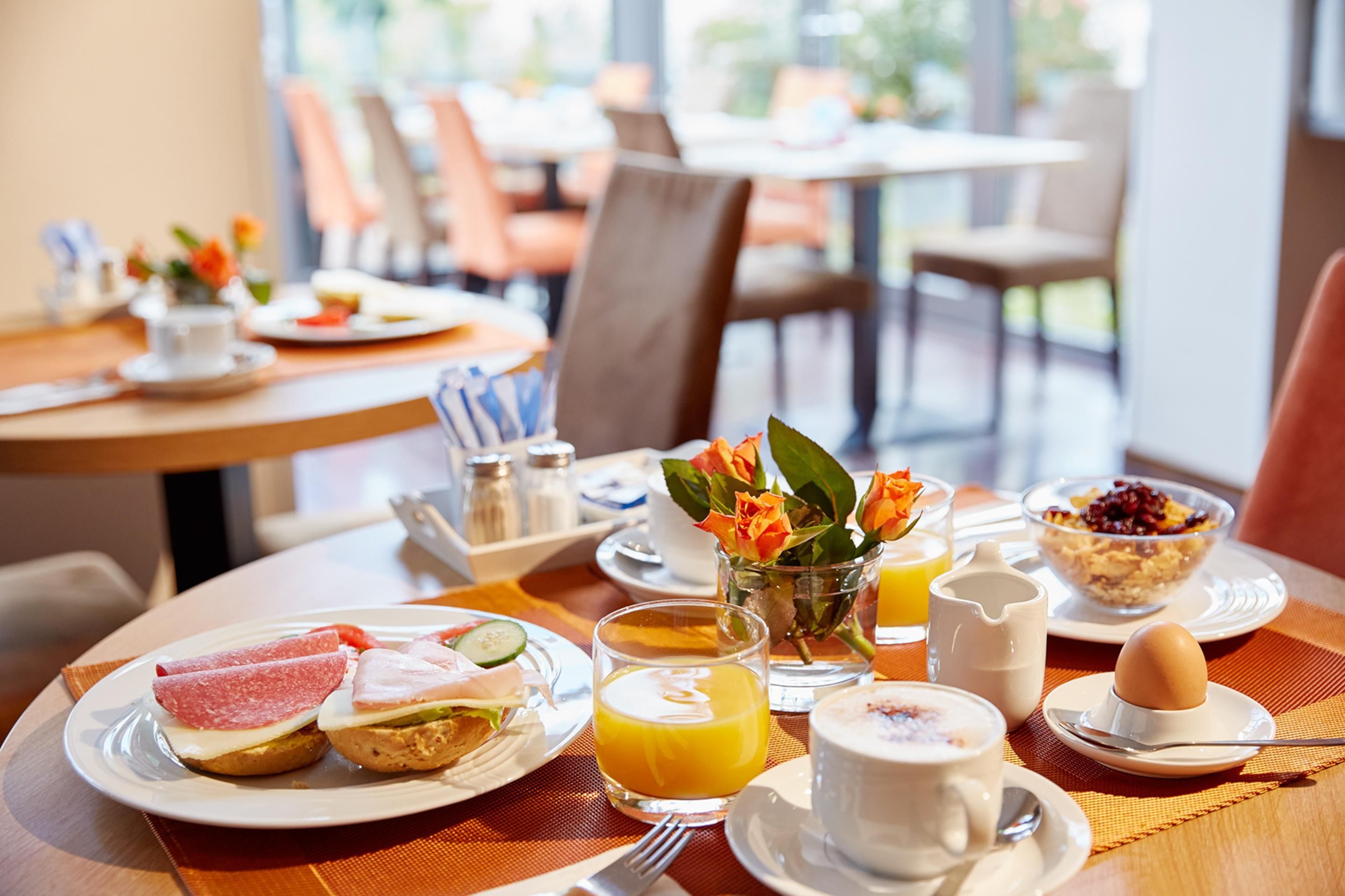 A breakfast setting with plates of food, a glass of orange juice, a cup of coffee, and a vase with flowers.