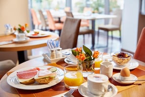 A breakfast setting with plates of food, a glass of orange juice, a cup of coffee, and a vase with flowers. - Hotel Imperial Dusseldorf, Sure Collection by BW (Düsseldorf)