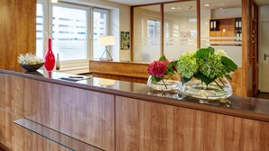 Et moderne receptionsområde med en træreception, en rød vase og to glasvaser med blomster.