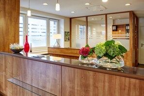A modern reception area with a wooden reception desk, a red vase, and two glass vases with flowers.