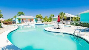 Ein Swimmingpool mit Liegestühlen und Sonnenschirmen, umgeben von Gebäuden und Palmen.