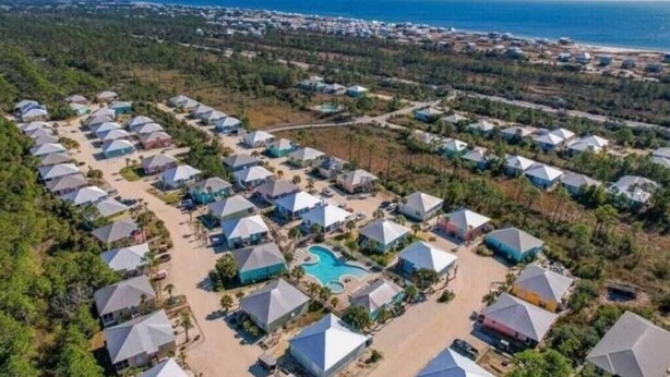 Eine Vogelperspektive zeigt ein Resort mit mehreren kuppelartigen Gebäuden, einem zentralen Schwimmbecken und einem Strand im Hintergrund.