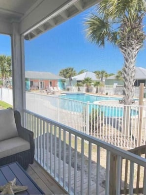 A covered outdoor area with a pool, palm trees, and a view of a building in the background.