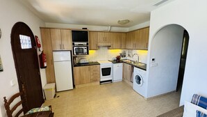 A compact kitchen with wooden cabinets, a refrigerator, a microwave, a stove, a sink, and a washing machine. - Apartment MULBERRY (Son Bou)