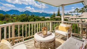 Ein Balkon mit Korbmöbeln, einer Laterne und Blick auf Berge und Grün.