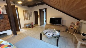 A cozy loft-style room with a sloped ceiling, a television, a small table with a lace tablecloth, and a colorful cushion. - Schöne, Geräumige Ferienwohnung im Wein- u. Wandergebiet, Freizeitpark I.d. Nähe (Löchgau)